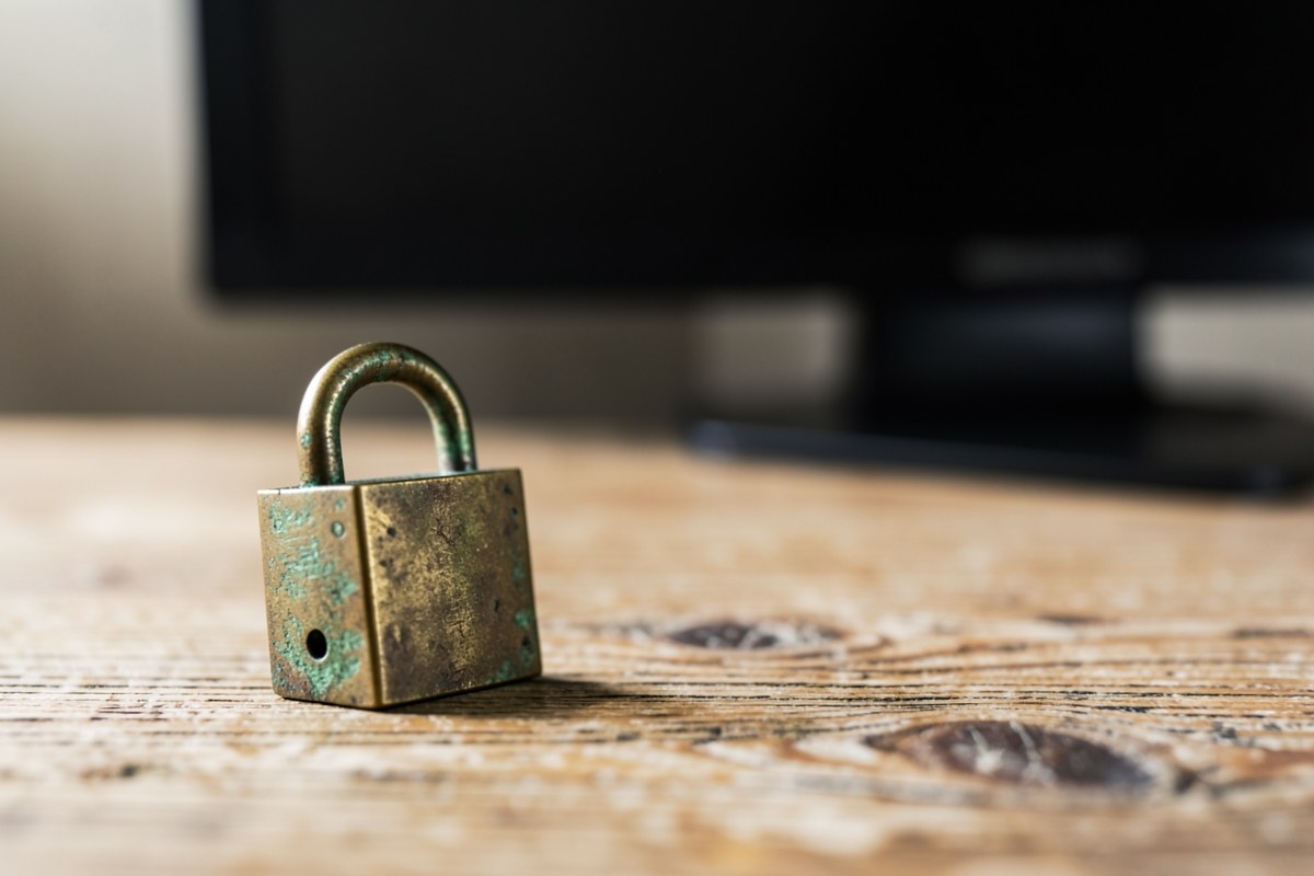 A closed padlock on a wooden surface, with a blurred background of a computer monitor, symbolizing data security.